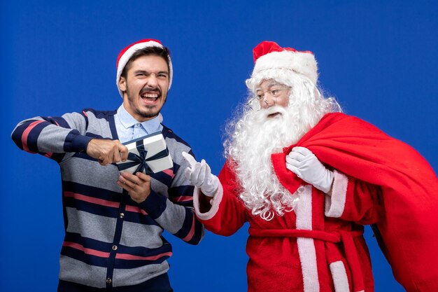 Vooraanzicht van de kerstman met jonge man die aanwezig is op de blauwe muur