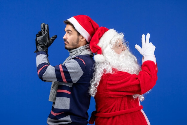 Vooraanzicht van de kerstman met jonge man die zich voordeed op de blauwe muur