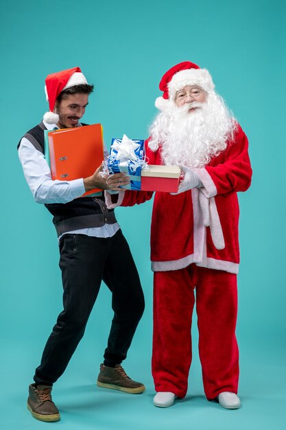 Vooraanzicht van de kerstman met jonge man en cadeautjes op blauwe muur