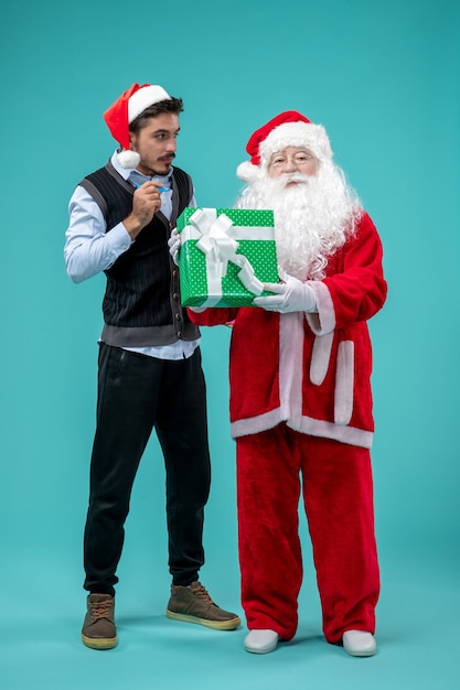 Gratis foto vooraanzicht van de kerstman met jonge man en vakantie aanwezig op de blauwe muur