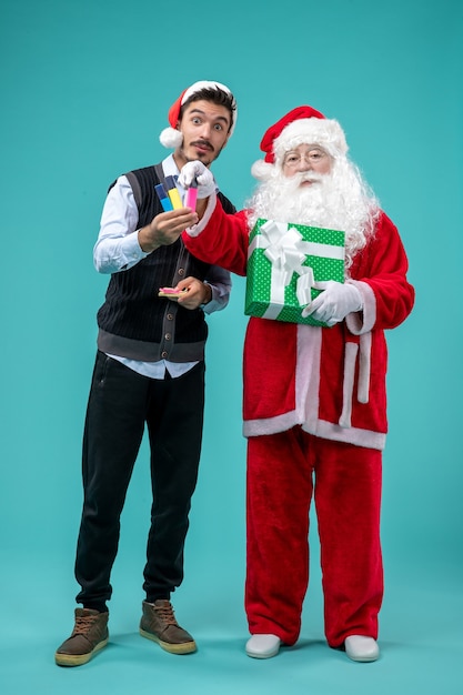 Vooraanzicht van de kerstman met jonge man en vakantie aanwezig op de blauwe muur