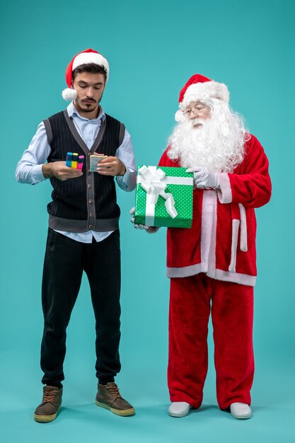 Vooraanzicht van de kerstman met jonge man en vakantie presenteert op de blauwe muur