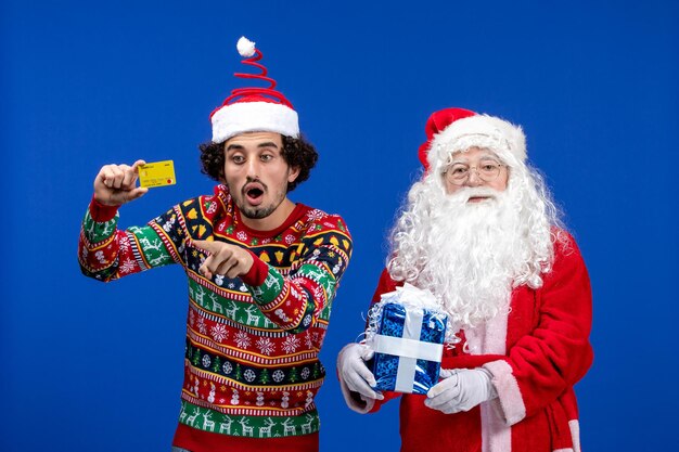 Vooraanzicht van de kerstman met jonge man met bankkaart en aanwezig op de blauwe muur