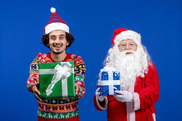 Vooraanzicht van de kerstman met jonge man met kerstcadeautjes op de blauwe muur