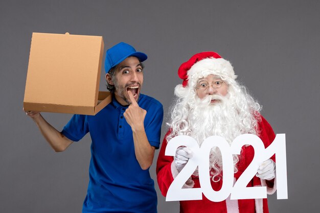 Vooraanzicht van de kerstman met mannelijke koerier die 2021 banner en voedseldoos op grijze muur houdt