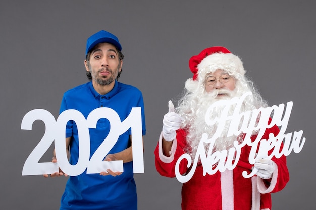 Vooraanzicht van de kerstman met mannelijke koerier die gelukkig nieuwjaar en 2021-planken op de grijze muur houdt