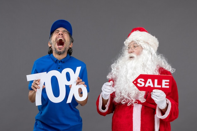 Vooraanzicht van de kerstman met mannelijke koerier die verkoopbanners op de grijze muur houdt