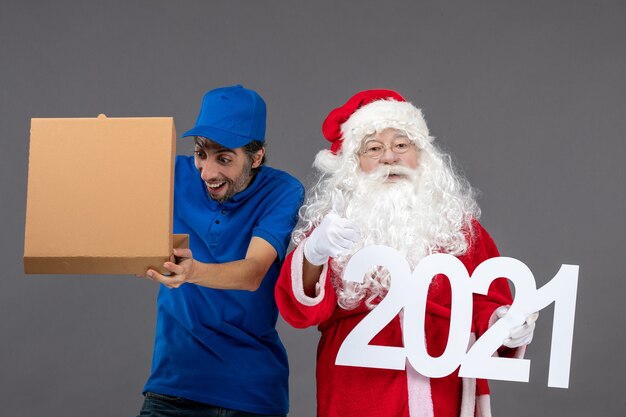 Vooraanzicht van de kerstman met mannelijke koerier die voedseldoos houdt en op de grijze muur schrijft