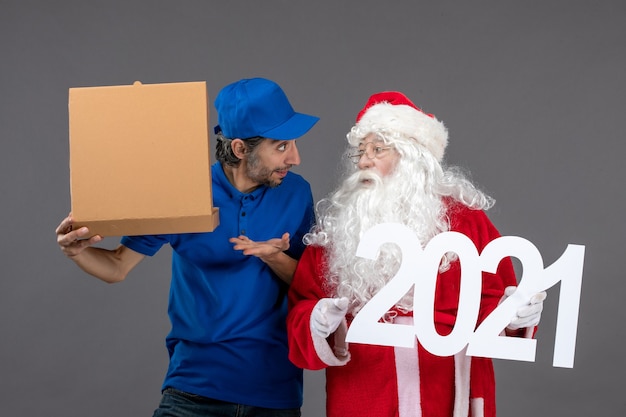 Gratis foto vooraanzicht van de kerstman met mannelijke koerier met voedseldoos en op de grijze muur