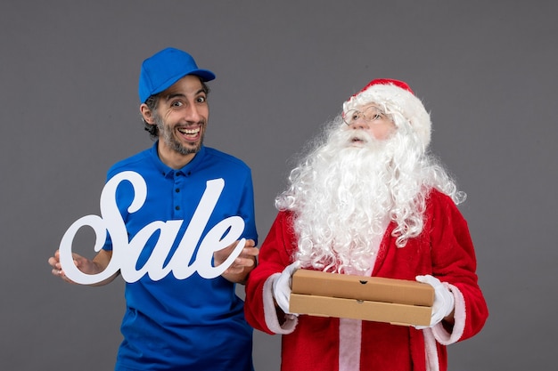 Vooraanzicht van de kerstman met mannelijke koeriersbedrijf verkoop banner en voedseldozen op de grijze muur