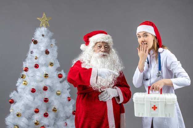 Vooraanzicht van de kerstman met vrouwelijke arts die ehbo-doos op de grijze muur houdt