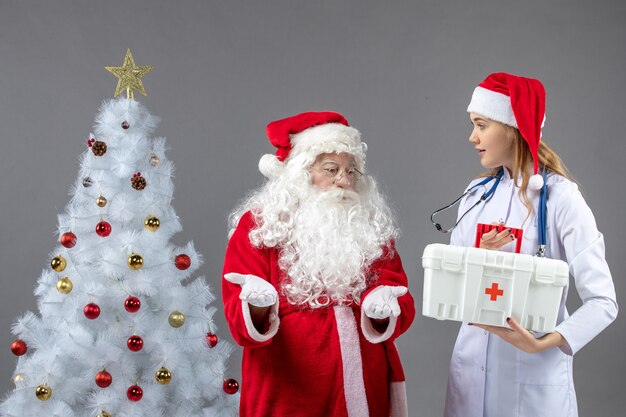 Vooraanzicht van de kerstman met vrouwelijke arts die EHBO-doos op de grijze muur houdt