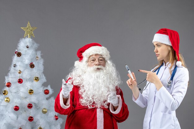 Vooraanzicht van de kerstman met vrouwelijke arts die injectie op de grijze muur houdt