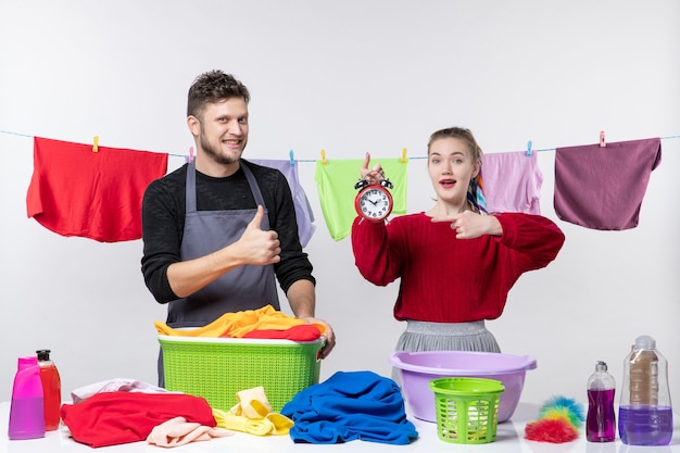 Vooraanzicht van de man die duim omhoog tekent en zijn vrouw wijzend op de wekker die achter tafelwasmanden staat en spullen op tafel wast