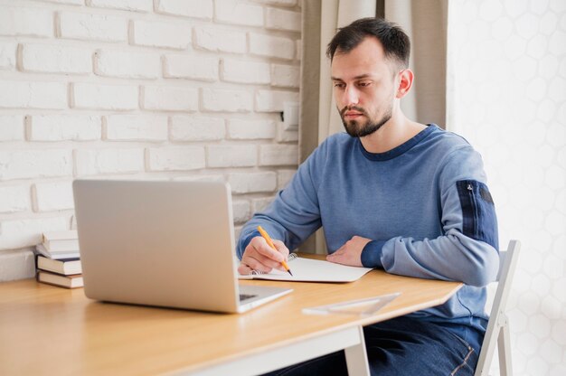 Vooraanzicht van de mens bij bureau dat online van laptop leert