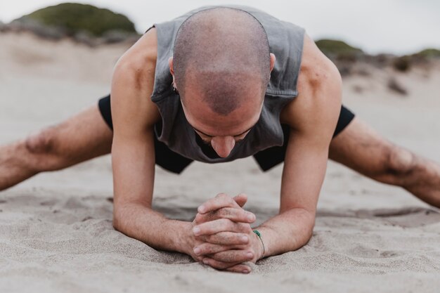 Vooraanzicht van de mens die op het strand yogahoudingen op zand uitoefent