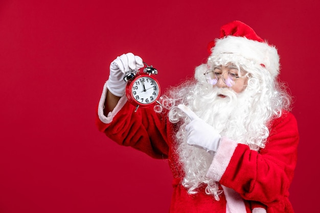 Vooraanzicht van de oude kerstman in rood pak met klok op de rode muur