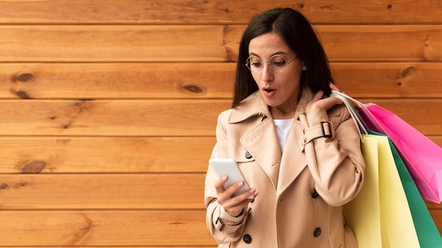 Gratis foto vooraanzicht van de vrouw die geschokt naar haar telefoon kijkt terwijl ze boodschappentassen vasthoudt