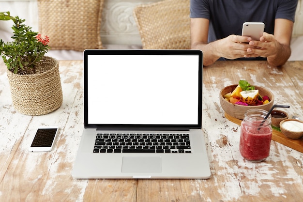 Vooraanzicht van de werkplek van zelfstandige vrouw of freelancer: generieke laptopcomputer rustend op houten tafel met slimme telefoon