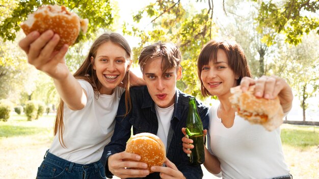 Vooraanzicht van drie vrienden in het park met hamburgers en bier