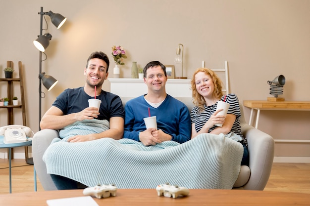 Vooraanzicht van drie vrienden op de sofa met deken en frisdrank cups