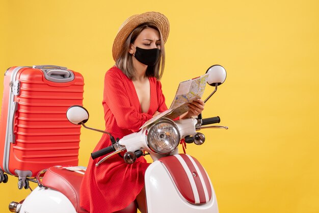 Vooraanzicht van drukke jonge dame die met zwart masker kaart dichtbij bromfiets bekijkt