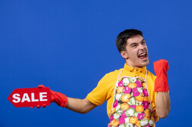 Gratis foto vooraanzicht van een dolblije mannelijke huishoudster in een geel t-shirt met een verkoopbord met geluk op de blauwe muur