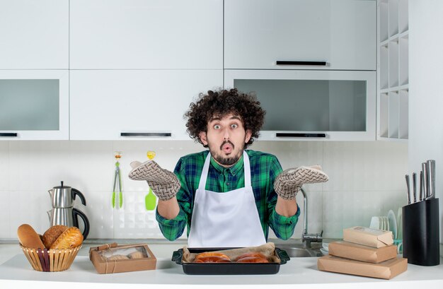 Vooraanzicht van een emotionele man met een houder die achter een tafel staat met versgebakken gebak erop in de witte keuken