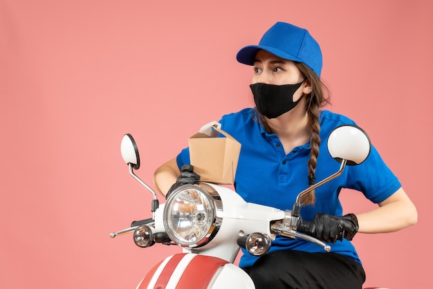 Vooraanzicht van een gefocuste vrouwelijke koerier met een zwart medisch masker en handschoenen met een kleine doos op een perzikachtergrond