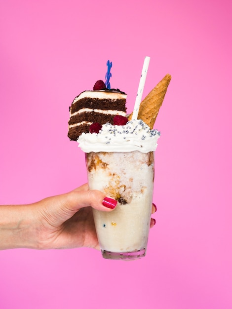Vooraanzicht van een hand die een milkshake met roze achtergrond houdt
