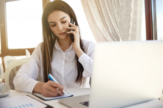 Vooraanzicht van een jonge aantrekkelijke langharige vrouw die met een cliënt op cellphone op het kantoor spreekt