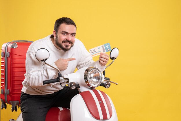 Vooraanzicht van een jonge glimlachende reizende man die op een motorfiets zit met een koffer erop met een kaartje op een geïsoleerde gele achtergrond