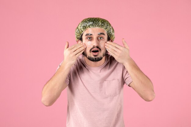 vooraanzicht van een jonge man die een masker op zijn gezicht op een roze muur aanbrengt