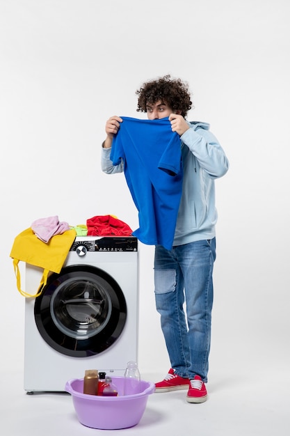 Vooraanzicht van een jonge man die schone kleren uit de wasmachine haalt en aan de witte muur ruikt