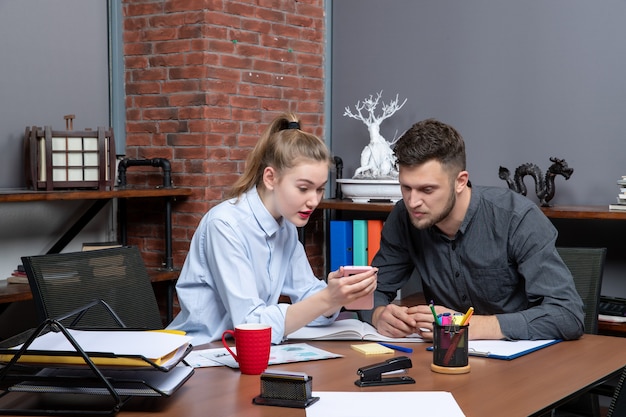 Vooraanzicht van een jonge man en zijn vrouwelijke collega die aan tafel zitten en één probleem bespreken in een kantooromgeving