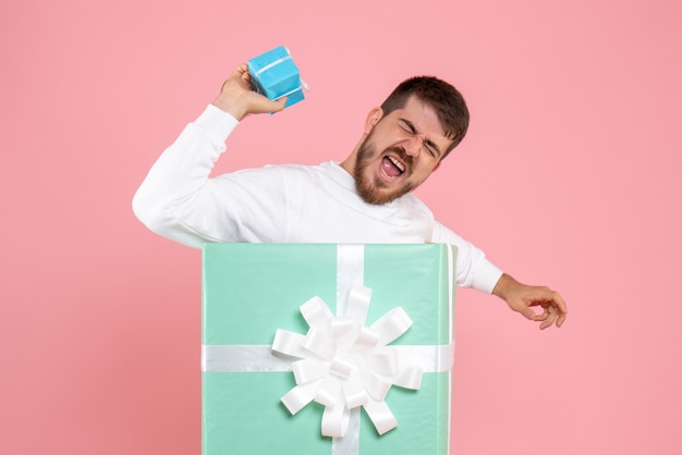 Vooraanzicht van een jonge man in de huidige doos met een klein cadeautje op de roze muur