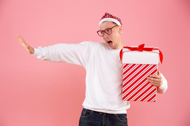 Vooraanzicht van een jonge man met een groot cadeau op de roze muur