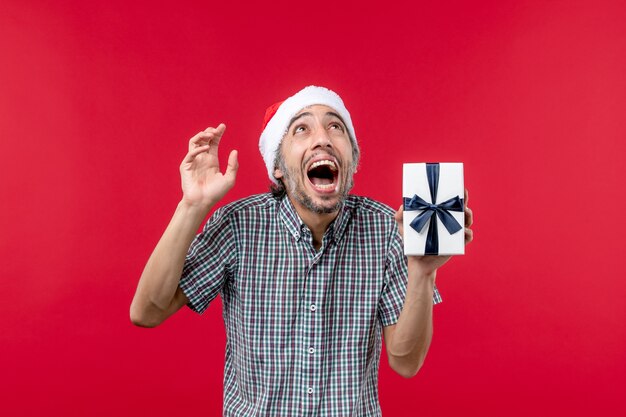 Vooraanzicht van een jonge man met een klein cadeautje op rood