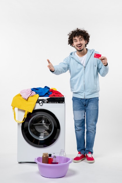 Vooraanzicht van een jonge man met een wasmachine die een rode bankkaart vasthoudt en iemand begroet op een witte muur