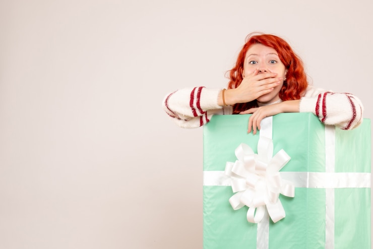 Gratis Foto vooraanzicht van een jonge vrouw die zich binnen kerstmis op witte muur verbergt