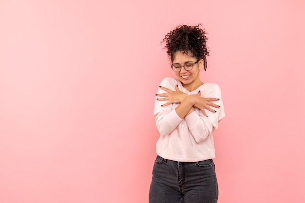 Gratis foto vooraanzicht van een jonge vrouw die zichzelf knuffelt op een roze muur