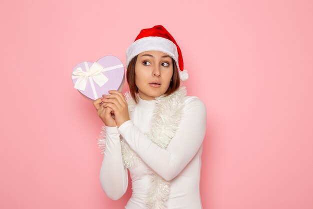 Gratis foto vooraanzicht van een jonge vrouw met een rode dop met een hartvormig cadeau op de roze muur