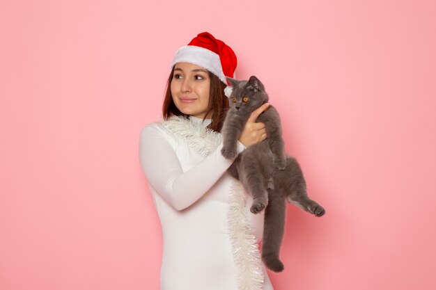 Vooraanzicht van een jonge vrouw met een rode dop met een schattig grijs katje op de roze muur