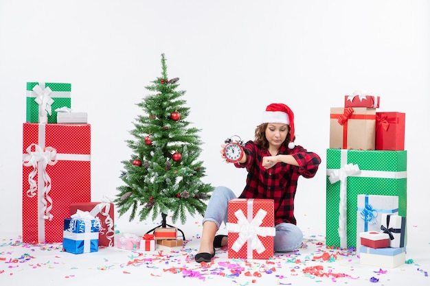 Vooraanzicht van een jonge vrouw rond kerstcadeautjes zitten met klokken op de witte muur