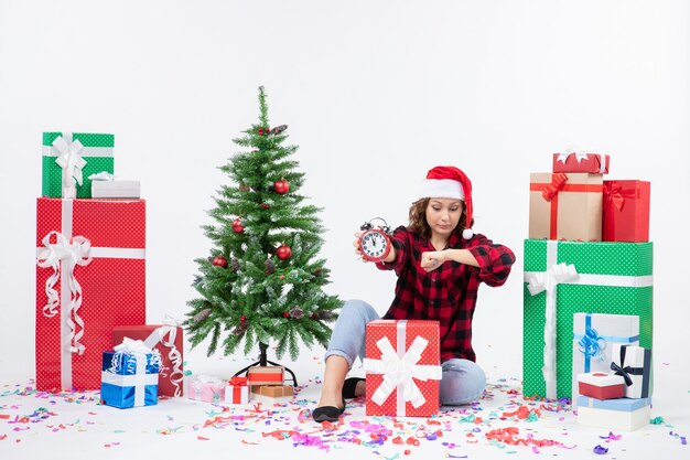 Vooraanzicht van een jonge vrouw rond kerstcadeautjes zitten met klokken op de witte muur