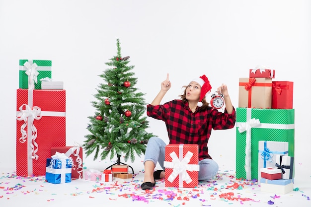 Vooraanzicht van een jonge vrouw rond kerstcadeautjes zitten met klokken op de witte muur