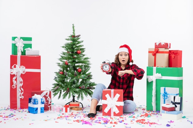 Vooraanzicht van een jonge vrouw rond kerstcadeautjes zitten met klokken op de witte muur