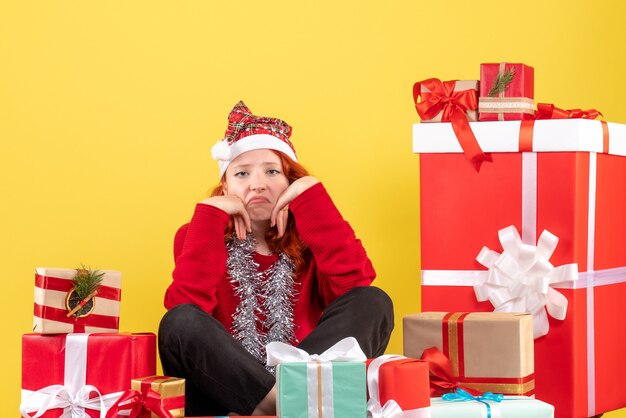 Vooraanzicht van een jonge vrouw rond kerstcadeautjes zitten vervelen op een gele muur