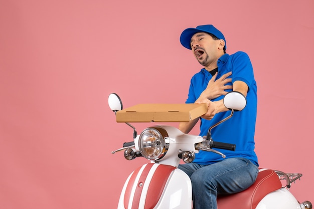 Vooraanzicht van een koeriersman met een hoed die op een scooter zit en lijdt aan een hartaanval op een pastelkleurige perzikachtergrond