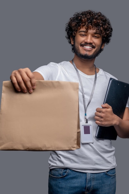 Vooraanzicht van een tevreden bezorger met een ID-badge met een dossiermap en een papieren zak